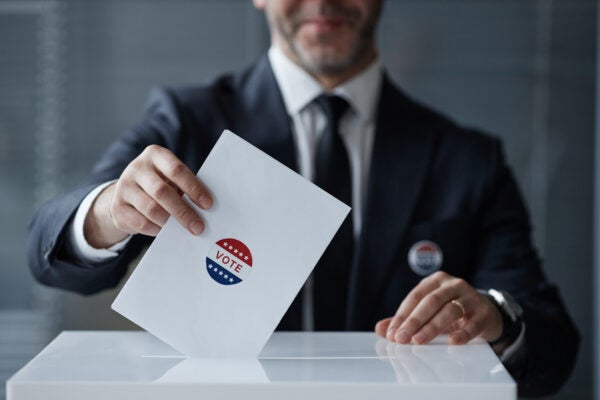 A man in a suit drops a voting envelope with a 