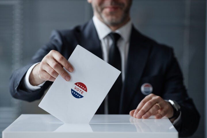 A man in a suit drops a voting envelope with a 